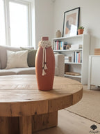 A matte terracotta bottle vase adorned with multi-strand jute tassels and alternating wood bead textures.