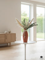 A matte terracotta bottle vase adorned with multi-strand jute tassels and alternating wood bead textures.